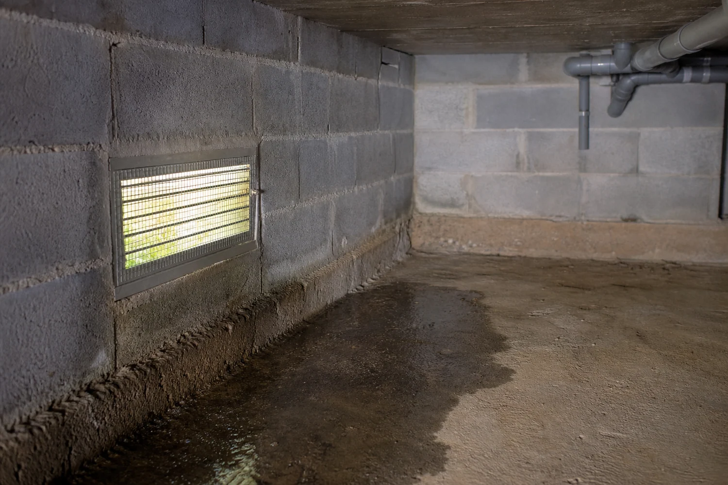 Ouverture de ventilation et sol humide visibles dans un vide sanitaire maçonné